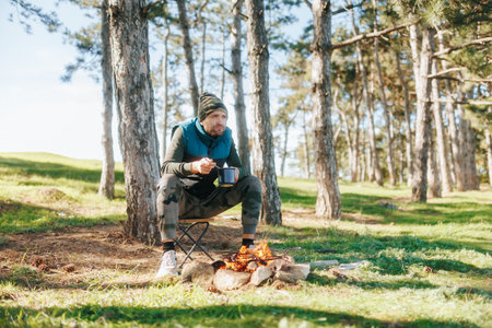 Seated Next to a Campfire, a Man Eats from a Pot in the Forestの写真素材