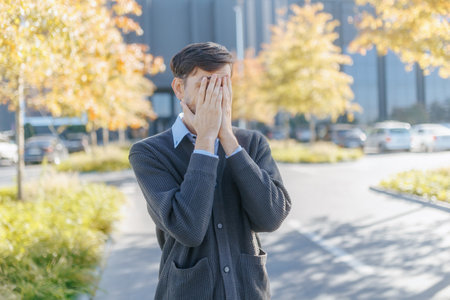 Stressed Office Worker Covering Face in Moment of Despair Outdoorsの写真素材