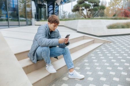 Teenage boy relaxing, enjoying music in city with phone in handの写真素材