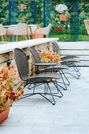 Wicker patio chairs with a table, stone wall, and vibrant garden plants.