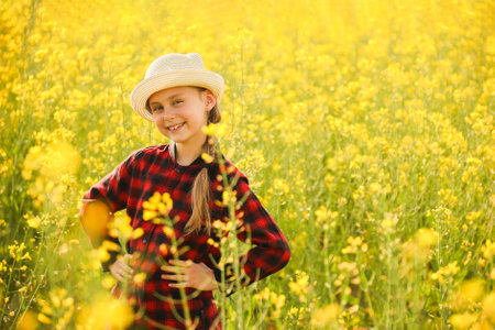 Portrait of a young girl in plaid dress in a sunlit yellow flower field.の写真素材