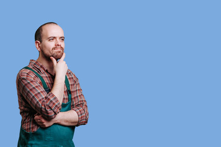 Man in green apron pondering against blue backgroundの写真素材