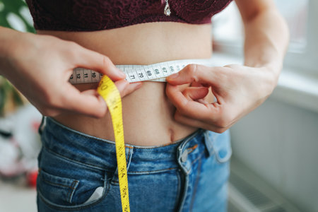 Woman measures waist with a tape measure indoors during daylight hoursの写真素材