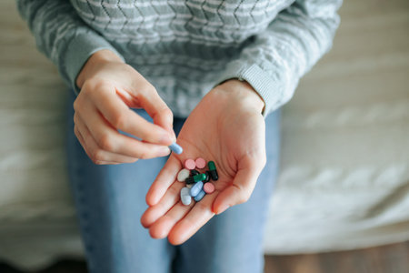 Individual sorting through various pills in a home setting during daytimeの写真素材