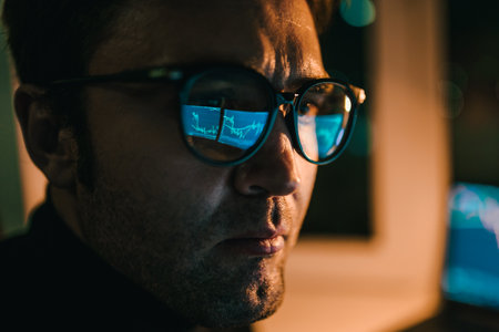 Man focused on computer screen displaying charts during the nightの写真素材