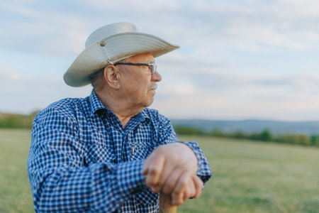 Old farmer stands in stillness as the golden light fades behind the hills, embodying the timeless grit and soul of rural cowboy life.の写真素材