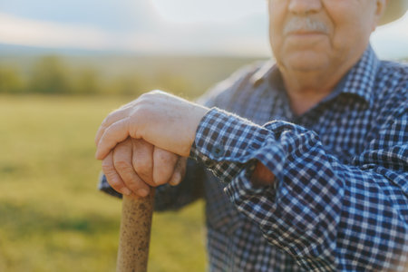 Close-up of senior farmer weathered hands resting on a shovel in a sunlit field, capturing a quiet, reflective moment after a long day of work outdoors.の写真素材