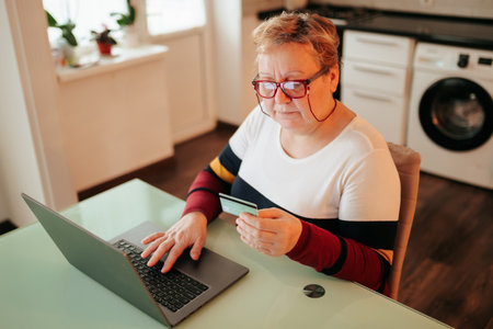 Senior woman using laptop at home while holding credit card and shopping onlineの写真素材