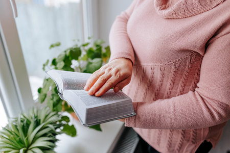 Woman reading a book near a window with plants during daytimeの写真素材