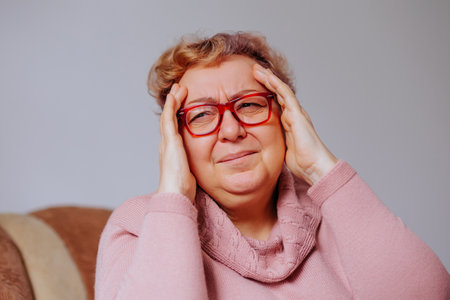 Middle-aged woman experiencing discomfort and stress while sitting indoorsの写真素材