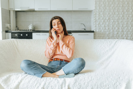 Woman sitting on a couch in a cozy kitchen while talking on the phoneの写真素材