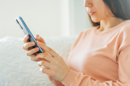 Young woman engaged in texting while sitting on a cozy couch at homeの写真素材
