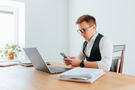 Professional man focused on smartphone while working at desk in officeの写真素材