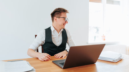 Young professional engaged in work at a wooden desk in a bright office spaceの写真素材