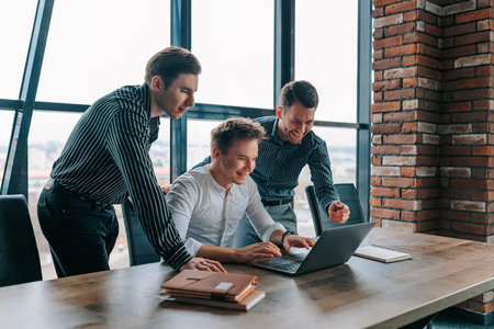 Young businessmen celebrate project success together in modern office environment while working on...