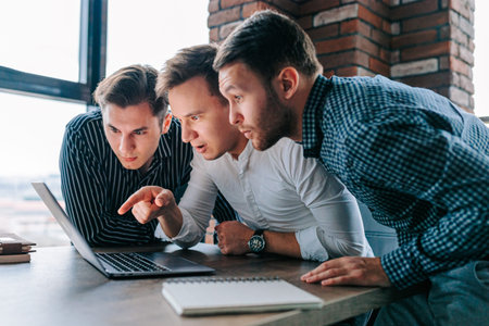 Men amazed at laptops while working diligently in a busy office environment during the dayの写真素材