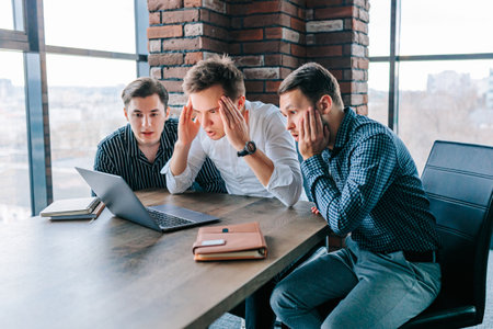Young men in office express bewilderment over challenging laptop tasks and discoveriesの写真素材
