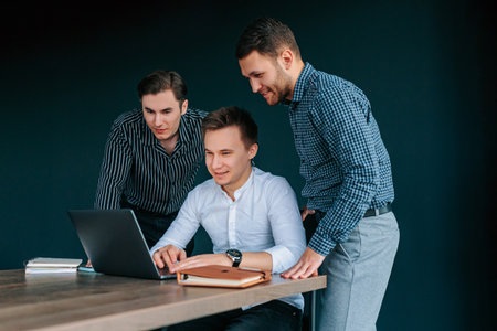 Group of young businessmen in suits collaborate on future plans with laptops in modern office settingの写真素材