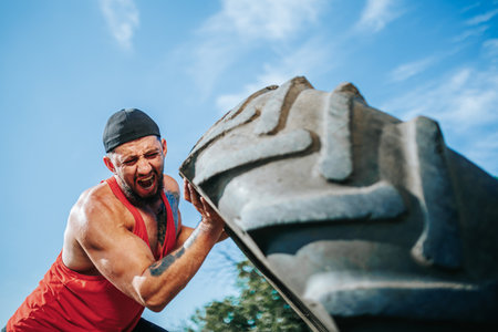 Man lifting heavy tire outdoors during workout session in bright sunlightの写真素材