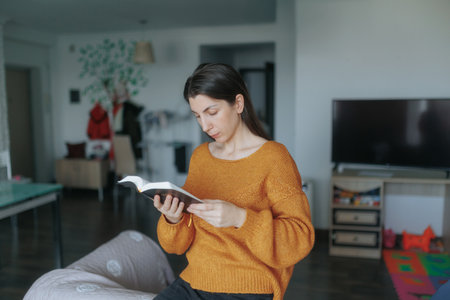 Young brunette woman reading a book in her modern kitchen at homeの写真素材