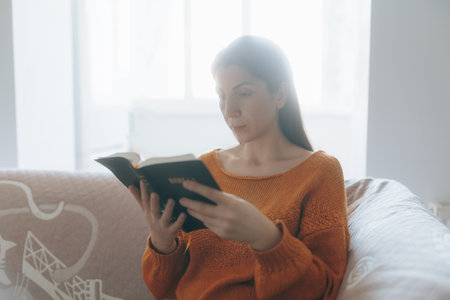Young woman spending time with a book at home, seeking inner peaceの写真素材