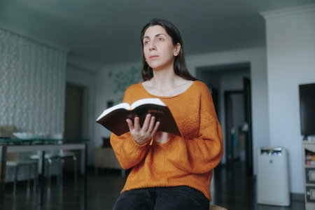 Young woman enjoying a quiet moment of reading at home in natural lightの写真素材