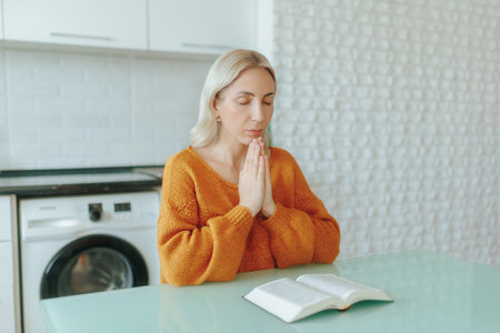 Serene woman sitting in her bedroom, praying and reading with devotion.の写真素材