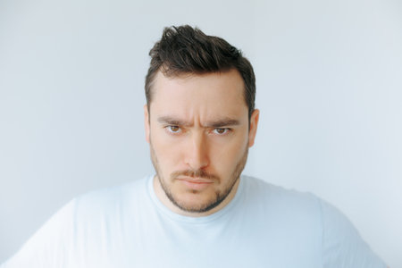 Serious man in plain shirt with intense expression against light backgroundの写真素材