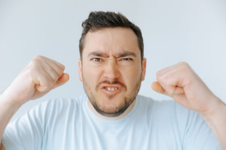 Frustrated man expressing anger with clenched fists in a neutral setting
