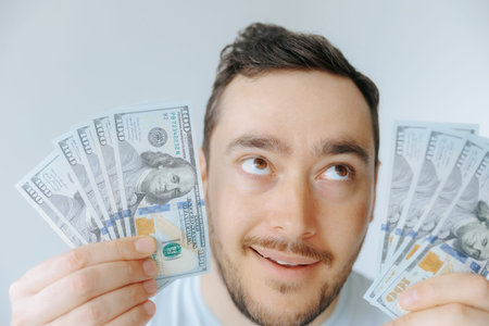 Man smiles while holding multiple hundred dollar bills in a bright settingの写真素材