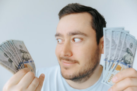Man holding cash with a thoughtful expression enjoying a financial momentの写真素材