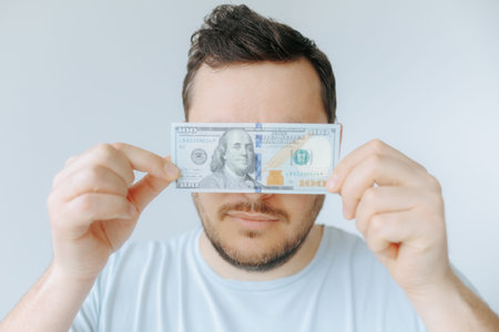 Man holds hundred-dollar bill in front of his face indoorsの写真素材