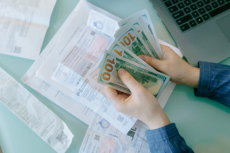 Managing finances with cash and bills on a desk during daytime work hoursの写真素材