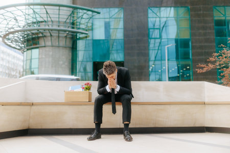 Man facing job loss struggles with emotions outside office buildingの写真素材