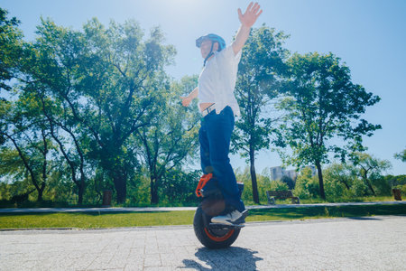 Stylish Man Enjoys Electric Monowheel Ride in Tree-Lined Parkの写真素材