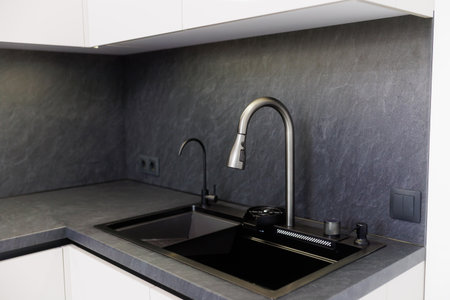 Modern kitchen with sleek faucet and dark countertops showcases contemporary design elementsの写真素材