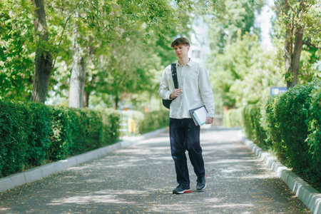 Teen boy walks alone outside school in spring, holding books