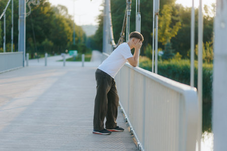 Teenager Emotionally Distraught and Alone on Bridge at Golden Hourの写真素材