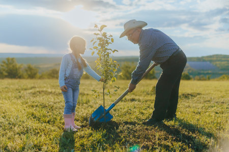 Little Girl and Her Grandfather Planting a Tree on a Sunny Dayの写真素材