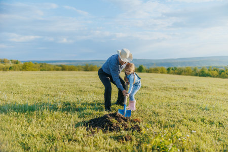 Grandfather and Granddaughter Planting Tree in Scenic Countrysideの写真素材