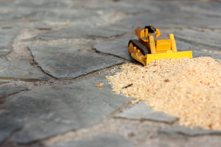 Toy bulldozer pushes a bunch of sawdust on the stones