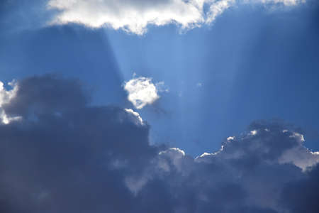 The sun's rays peek through the rain clouds. Rain clouds on a summer day have blocked out the sun and bright sun rays are breaking through the clouds.の写真素材