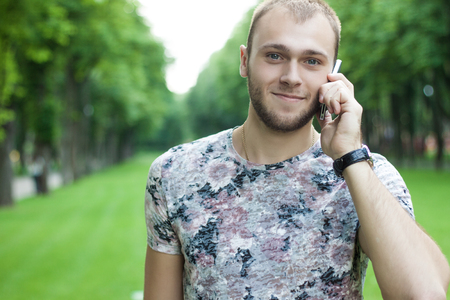 a handsome man talking on the phone in a garden. green Garden.Handsome man cell phone call smile outdoor city street, Young attractive businessman casual blue shirt talkingの写真素材