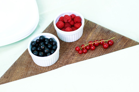 Assortment of berries - raspberries, gooseberries, red currants, cherries, black currants on a white plate on a wooden background. Healthy food, delicious summer dessertの写真素材