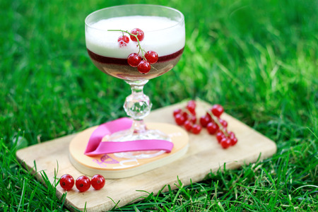 milk cocktail with black currant, red currant, banana, raspberries and ice cream. glass on a beautiful stand. sprigs of red currants on a background of grassの写真素材