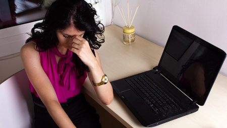 Business woman enduring headaches at her office beside her laptop.