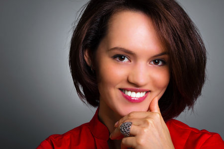 Close up portrait of a beautiful smiling woman with hand on chin, studio shoot, gray background.