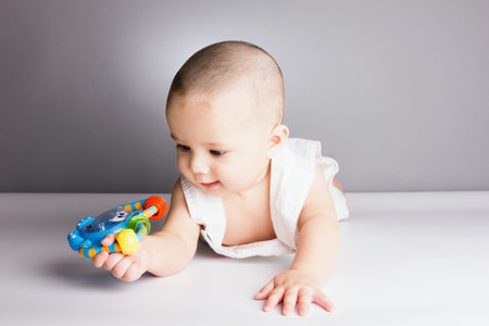 Happy baby boy staring at his toy, sitting on the floor, studio shooting.