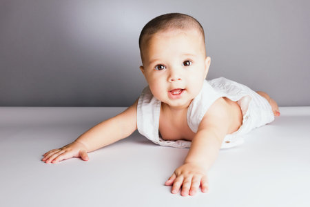 Gorgeous baby sitting on the floor, laughing shows his first teeth, studio shoot.