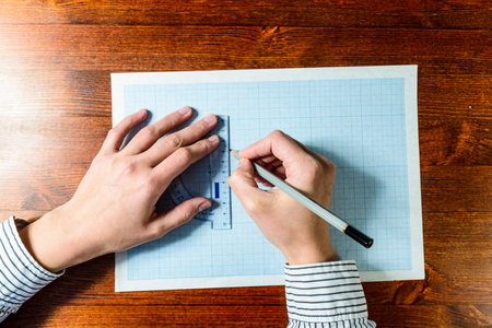 Female hands drawing with a pencil on a blue graph paper on wooden background